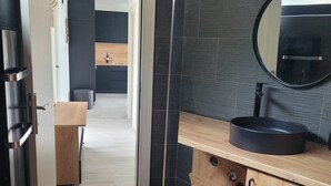 A modern kitchen with a wooden countertop, a black sink, and a round mirror.