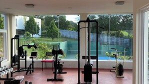 Een sportschool met diverse trainingsapparatuur, grote ramen en uitzicht op groen.