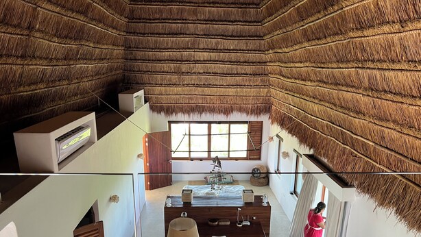 Una habitación con techo de paja, una cama, un escritorio y una ventana con cortinas.