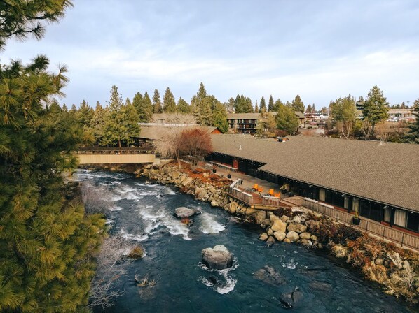A riverside hotel with a stone bridge, outdoor seating, and a view of the river.