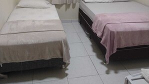 Une petite chambre propre, avec deux lits simples, une fenêtre avec des rideaux et un climatiseur fixé au mur.