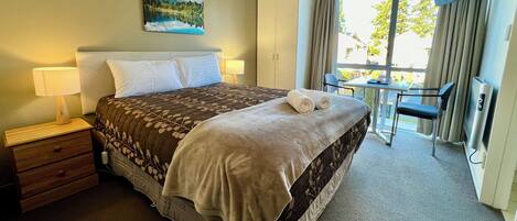 A hotel room with a bed, bedside tables, a desk, a chair, a TV, and a window with curtains.