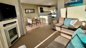 A modern living room with a flat-screen TV, a sofa, and a dining area with a table and chairs. - Brinkley Resort (Methven)