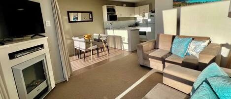 A modern living room with a flat-screen TV, a sofa, and a dining area with a table and chairs.
