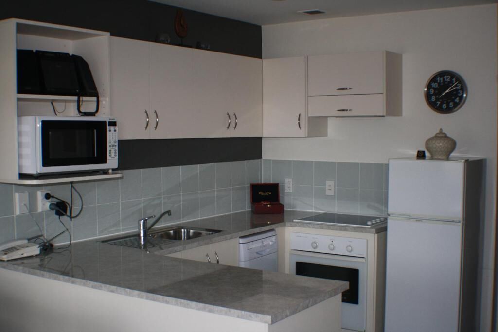 Une cuisine compacte avec des meubles blancs, un four à micro-ondes, une cuisinière, un lave-vaisselle et un réfrigérateur.