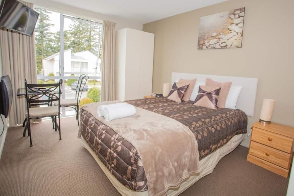Una habitación de hotel con cama, televisión, silla, escritorio y ventana con cortinas.