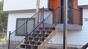 A two-story building with a white exterior and a wooden accent wall. There is a black staircase with a railing leading to a balcony.