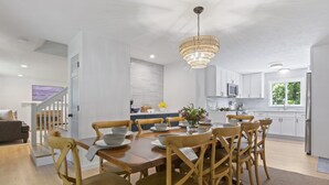 A modern kitchen with white cabinets, a wooden dining table, and a chandelier. - Trendy Great Pond Escape! HotTub Open! Sleeps 9! (Falmouth)