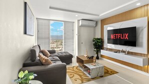Un salon moderne avec un canapé gris, une table basse en bois et un grand écran de télévision affichant le logo « NETFLIX ».