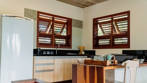 Una cocina con armarios de madera, un refrigerador, un lavamanos y una ventana con contraventanas de madera.