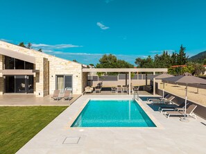 A modern outdoor pool area with a stone building, lounge chairs, and umbrellas.