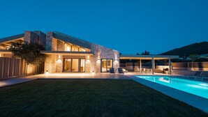 Una casa moderna con piscina, fachada de piedra y zona de estar exterior.