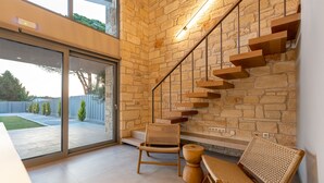 Un interior moderno con una escalera de pared de piedra, una puerta de cristal que da al exterior y dos sillas de mimbre.