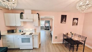 A modern kitchen with white cabinets, a built-in oven, and a dining area with a black table and chairs. - Audrey- an ode to an icon (Salem)