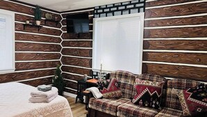 Une pièce chaleureuse avec un mur décoré de panneaux en bois, un canapé agrémenté de coussins à motifs, une petite table avec une lampe et un lit recouvert d’une couverture soigneusement pliée.