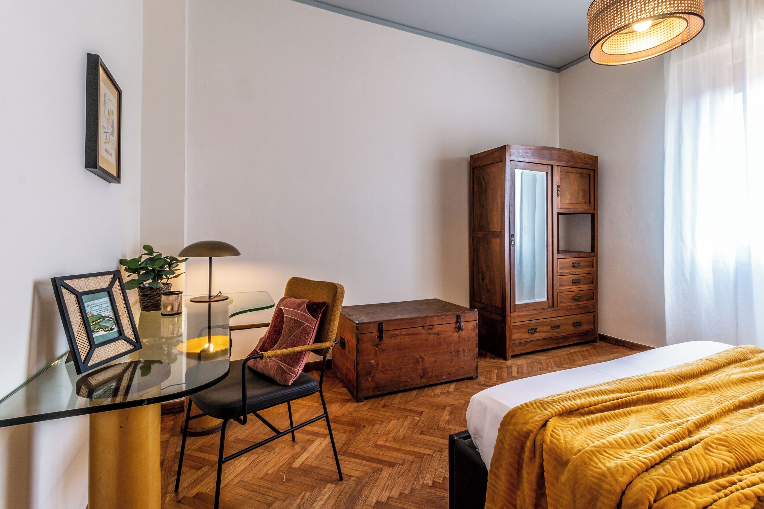 A room with a glass table, a chair, a wooden cabinet, and a bed.