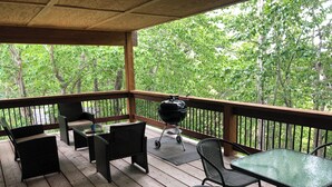 Eine überdachte Terrasse im Freien mit Holzboden, schwarzen Korbmöbeln und einem Grill.