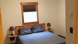 Ein Schlafzimmer mit einem Bett, zwei Nachttischen, einem Fenster mit Jalousien, einer Deckenleuchte und einem Thermostat.
