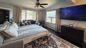 Un dormitorio con cama, ventilador de techo, televisor, cómoda y ventana con cortinas.