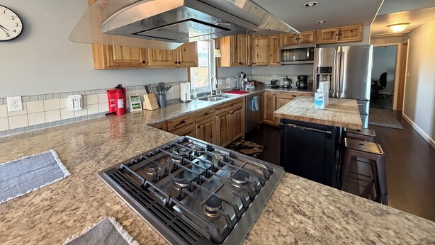 Una cocina moderna con encimeras de granito, electrodomésticos de acero inoxidable, armarios de madera y una estufa integrada.