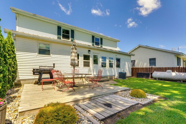 A two-story house with a patio area featuring a grill, red chairs, and a small garden. - Howe Retreat w/ Fire Pit + Private Boat Dock! (Howe)