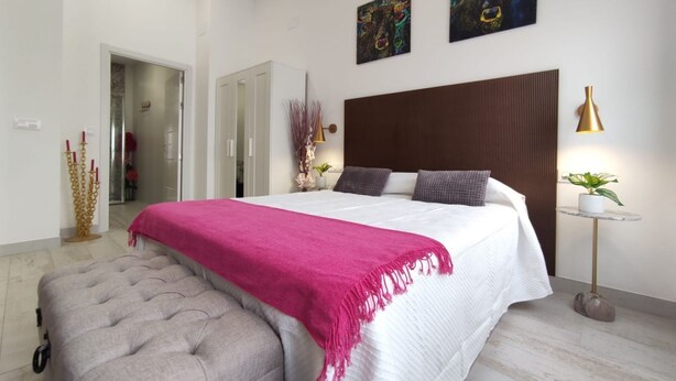 A bedroom with a large bed, a bedside table with a lamp, and two wall-mounted paintings. - The Urban Elegnace Suite (Sevilla)