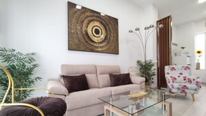 A modern living room with a beige sofa, a glass coffee table, a floral armchair, and a large abstract painting on the wall. - The Urban Elegnace Suite (Sevilla)