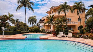 A swimming pool with lounge chairs and palm trees, surrounded by a building with balconies. - Paradise On Earth  (Boca Chica)