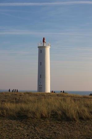 A lighthouse with a clear sky, situated on a grassy field with a few people in the distance.