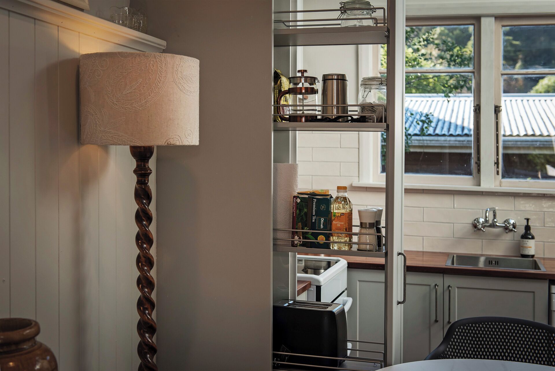 A kitchen with a wooden cabinet, a metal rack, and a window with a view of a house.