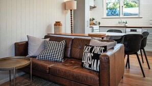 Ein gemütliches Wohnzimmer mit braunem Ledersofa, einem kleinen runden Tisch und einer Küche im Hintergrund.