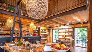 A rustic café interior with wooden beams, a bar area, and a view of greenery outside.