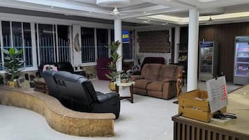 A modern lobby with a curved reception desk, leather sofas, a small table with a vase, and a refrigerator.