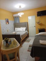 Habitación de hotel pequeña con cama, una mesita con un florero, un televisor en la pared y una puerta.