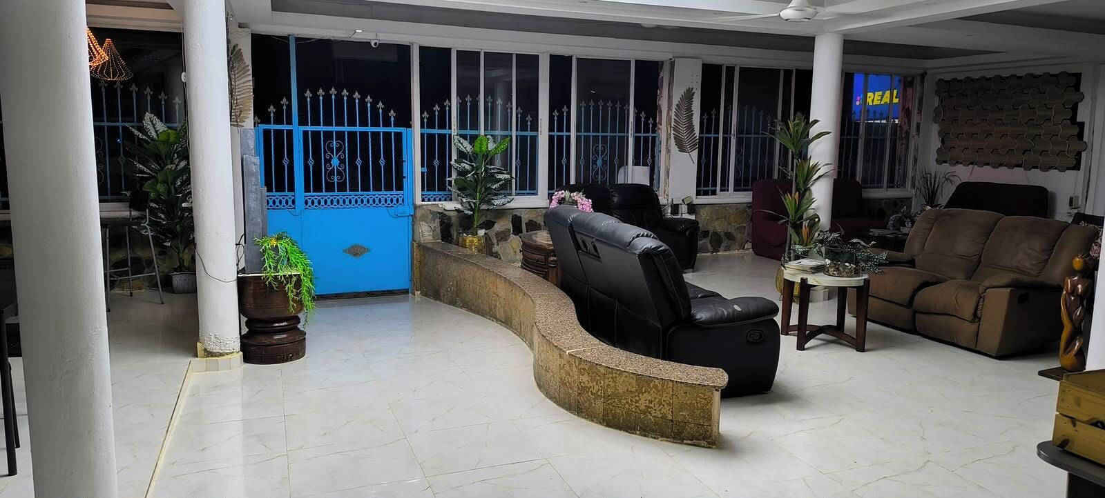 A spacious living area with a curved reception desk, a black leather sofa, and a brown recliner.