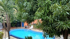 A swimming pool surrounded by greenery, with a tiled patio and lounge chairs. - Hotel Condo Mango (Boca Chica)