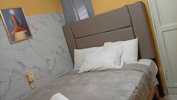 A hotel room with a bed, a bedside table, a towel, a wall-mounted air conditioner, a door, and a framed picture on the wall.