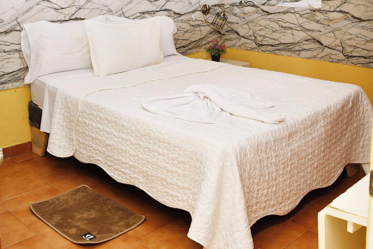 A hotel room with a bed, a marble-patterned wall, a yellow wall, and a ceiling light.