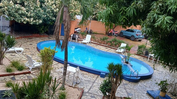 A swimming pool surrounded by palm trees and potted plants, with a stone pathway leading to a seating area. - Hotel Condo Mango (Boca Chica)