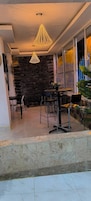 Un área de comedor al aire libre con un muro de piedra de fondo, una mesa con sillas y una lámpara colgante.