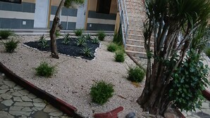 A multi-story building with numbered doors, a staircase, and a small garden area with plants and gravel. - Hotel Condo Mango (Boca Chica)