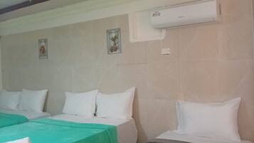 Habitación de hotel con dos camas, cada una con ropa blanca y un edredón verde en una de ellas. Se observa un equipo de aire acondicionado de pared sobre las camas.