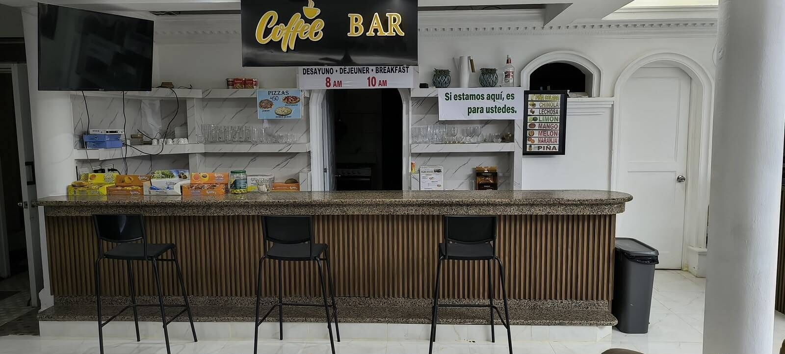 Un bar con un cartello che indica gli orari della colazione, una lavagna con offerte di caffè e cibo, e una televisione sopra il bancone.