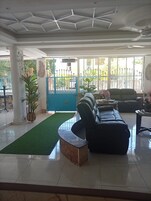 Amplia sala de estar con un banco curvo, un sofá y una mesa de centro. Se observa una reja azul y un ventanal con vistas al exterior.