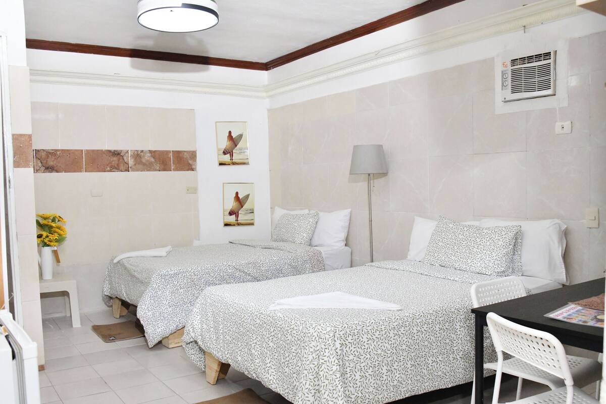 A hotel room with two beds, a desk, a chair, a lamp, and a small table.