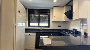 A modern kitchen with a built-in dishwasher, a black countertop, and white cabinets. - Asya Lara Suite (Antalya)
