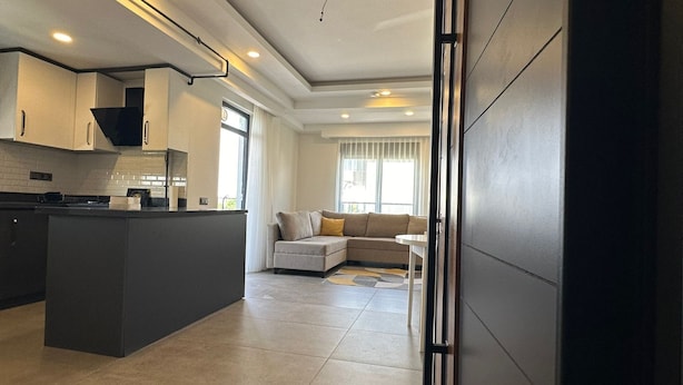 A modern kitchen with a central island, a dining area with a sofa, and a large window providing natural light. - Asya Lara Suite (Antalya)