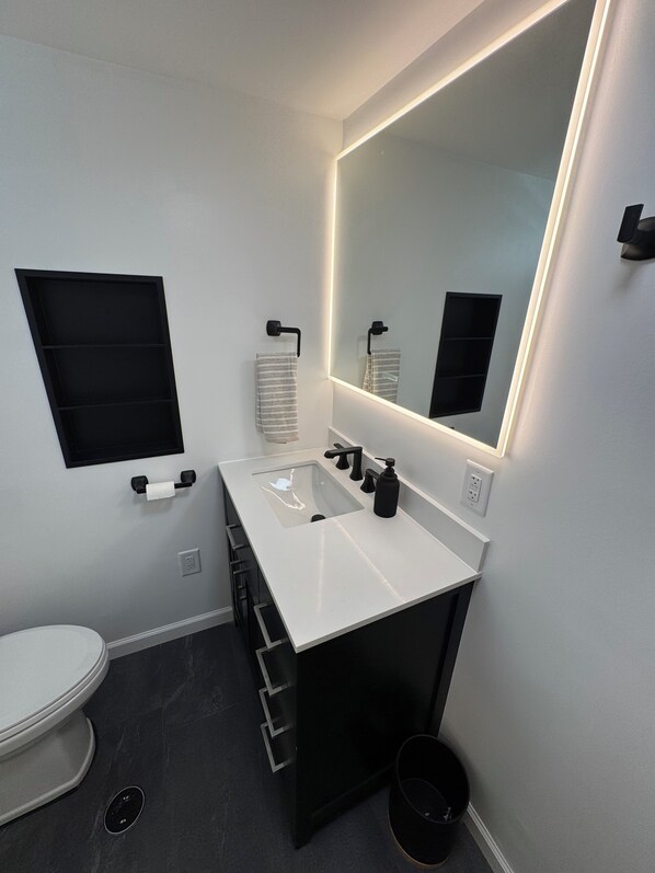 Une salle de bain moderne avec un lavabo blanc, un meuble-lavabo noir et un grand miroir.