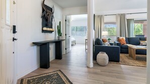 Un vaste espace de vie agrémenté d’un canapé bleu foncé, d’une table basse et d’un grand vase. Une console noire, sur laquelle est posée une plante, est adossée au mur.