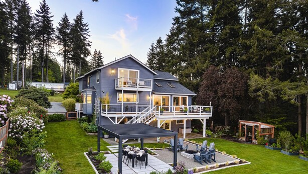 A two-story house with a balcony, a covered patio, and a well-maintained garden. - Puget Sound Waterfront | Eagles, Orcas & Mt. Rainier Views (Gig Harbor)